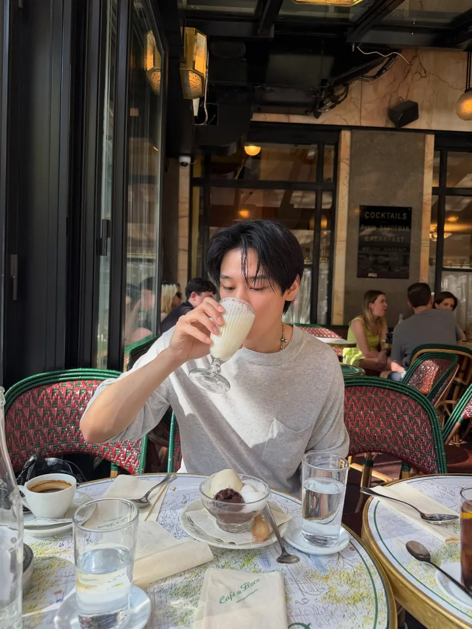 sadewa minum dari gelas di meja kafe dengan sweater abu-abu